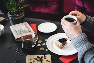 A cozy scene showing a hand holding a toffee coffee pack beside a steaming cup on a wooden table.
