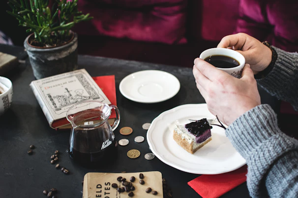 A cozy scene showing a hand holding a toffee coffee pack beside a steaming cup on a wooden table.