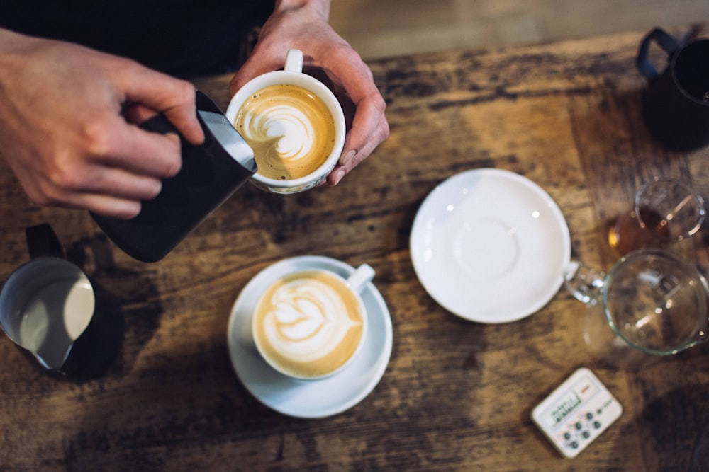 A person creating latte art at La Bohème Café over a wood table