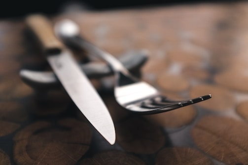 A close-up of a sleek, modern spoon and fork set resting on a rustic wooden table.