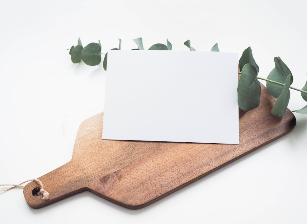 A wooden cutting board with a branch and piece of paper on top.