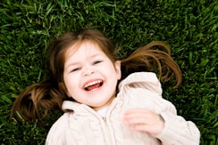 girl smiling while lying on grass field at daytime