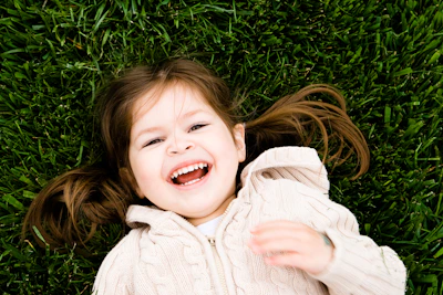 girl smiling while lying on grass field at daytime