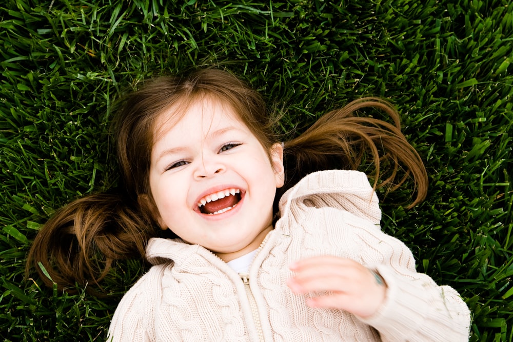 girl smiling while lying on grass field at daytime