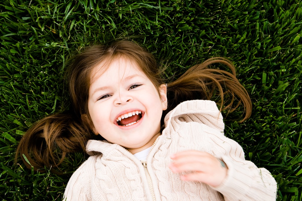 fille souriant tout en étant allongé sur le champ d’herbe pendant la journée