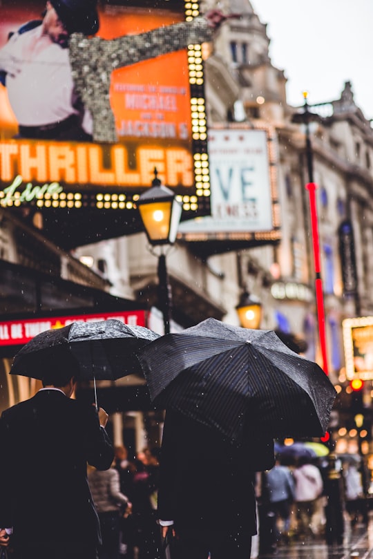 people walking while holding umbrella in Shaftesbury Avenue United Kingdom