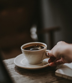 person holding white ceramic cup with liquid