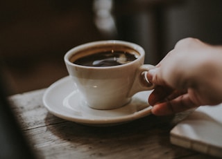 person holding white ceramic cup with liquid