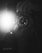 A black and white photograph captures a close-up of a person holding a camera with a lens in focus. The flash is prominently visible, causing a bright light in the image. The hands gripping the camera add an element of action and engagement.