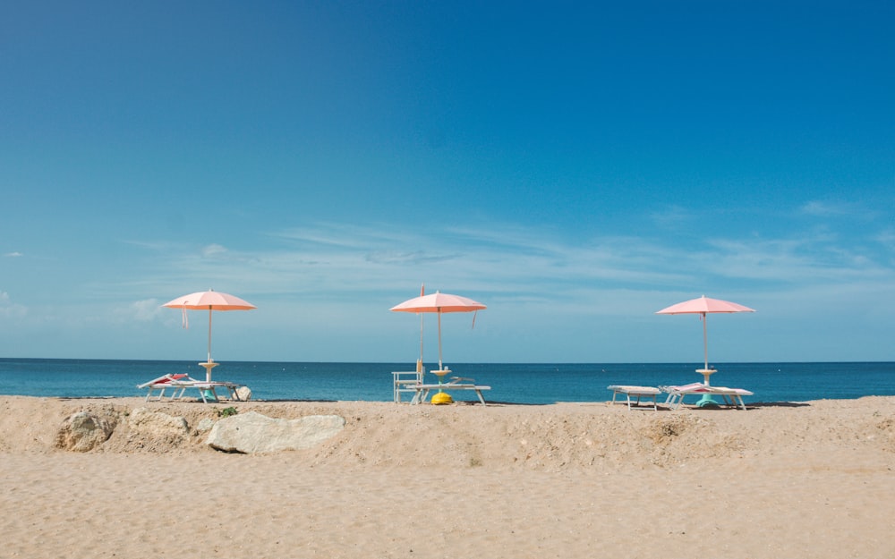 Drei leere Liegestühle mit Sonnenschirmen mit Blick auf den Strand unter blauem Himmel