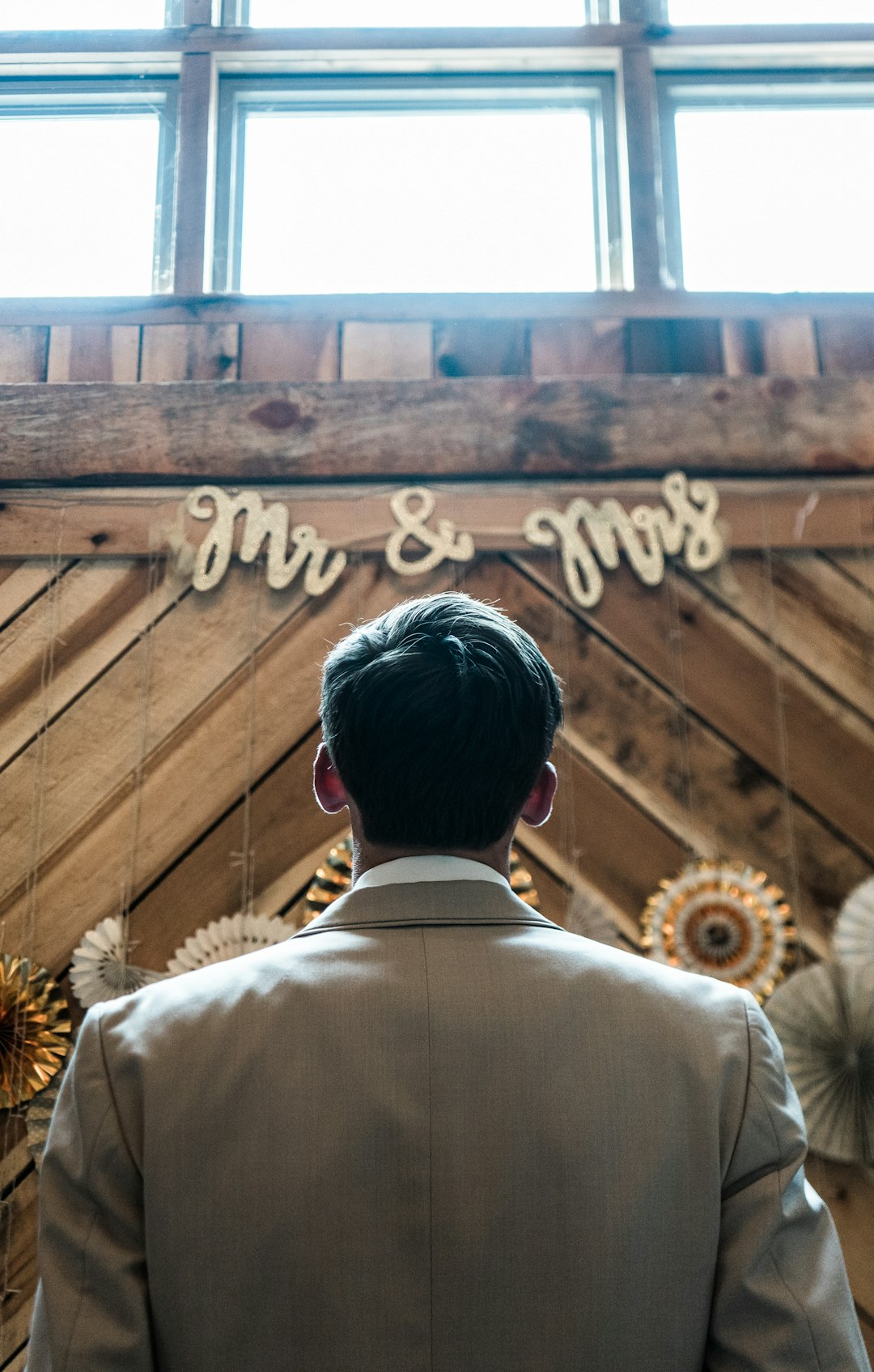 man in beige suit jacket standing in front of brown wooden wall