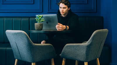 man sitting on couch with looking at his MacBook on table