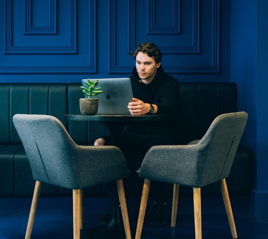 man sitting on couch with looking at his MacBook on table