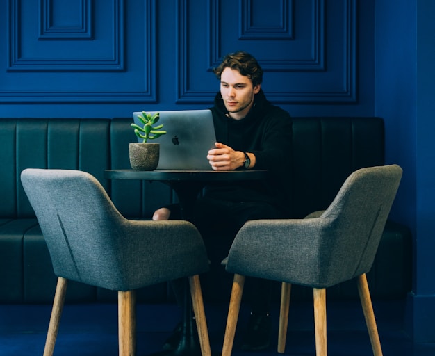 man sitting on couch with looking at his MacBook on table