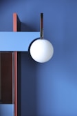 A modern interior featuring geometric shapes with a large white spherical light fixture hanging against a blue wall. There are contrasting vertical and horizontal elements in red and light blue, adding depth and structural interest.