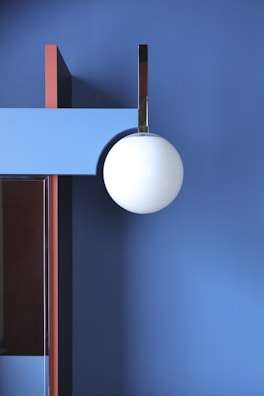 A modern interior featuring geometric shapes with a large white spherical light fixture hanging against a blue wall. There are contrasting vertical and horizontal elements in red and light blue, adding depth and structural interest.