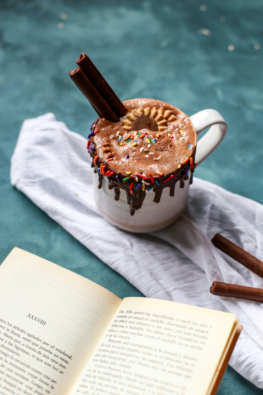 closeup photo of white mug full of chocolate drink with sprinkles and cookies