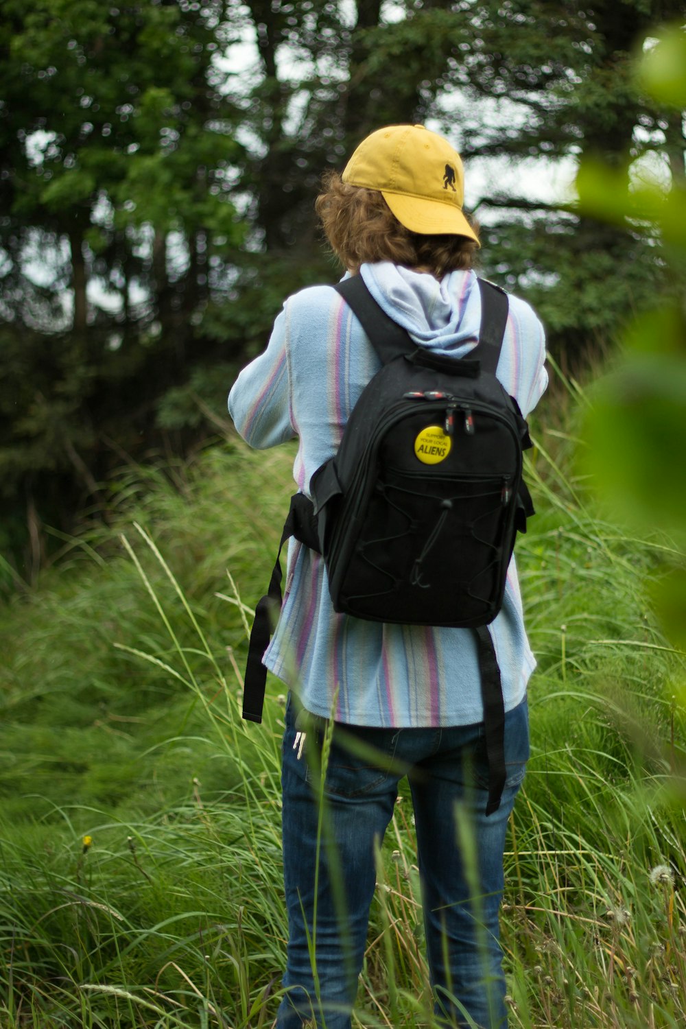 woman in gray hoodie and blue denim jeans with black backpack walking on green grass field