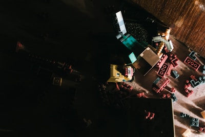 A dark and moody scene featuring scattered toy bricks and figurines, possibly resembling characters from a video game. The toys are primarily made up of red, yellow, blue, and green pieces, laying chaotically on a wooden surface.