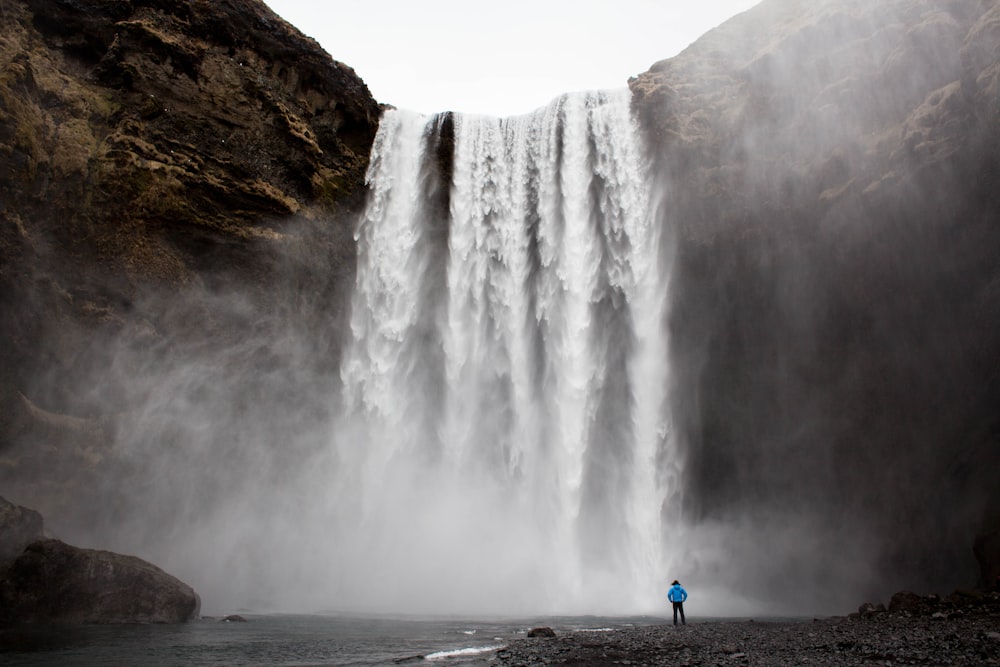 man standing front of waterfalls at daytime