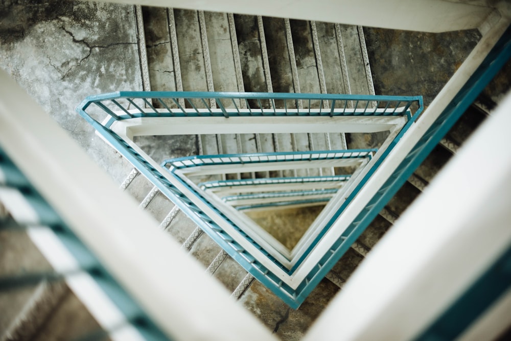 Looking down at the view of a triangular stairwell with teal-coloured handrails and slightly damaged steps