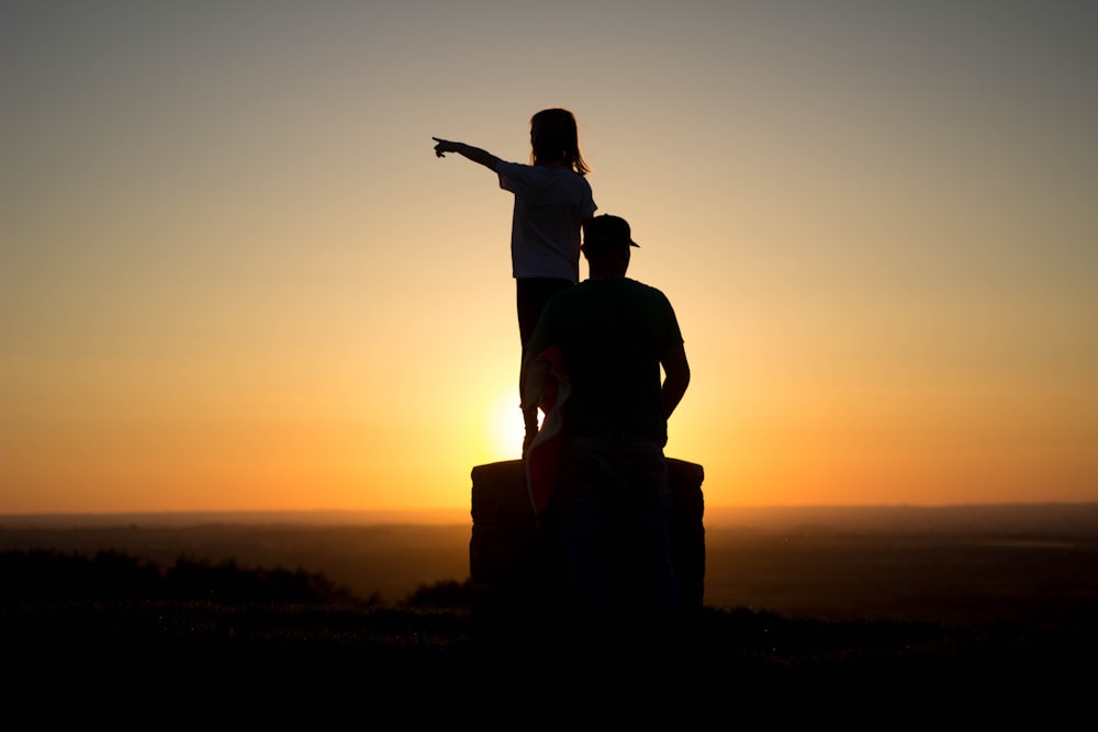 silhouette photo of two person sitting on cliff