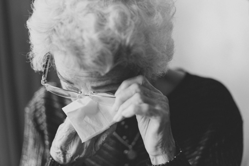 Old lady removing her spectacles to wipe her eye in black and white.