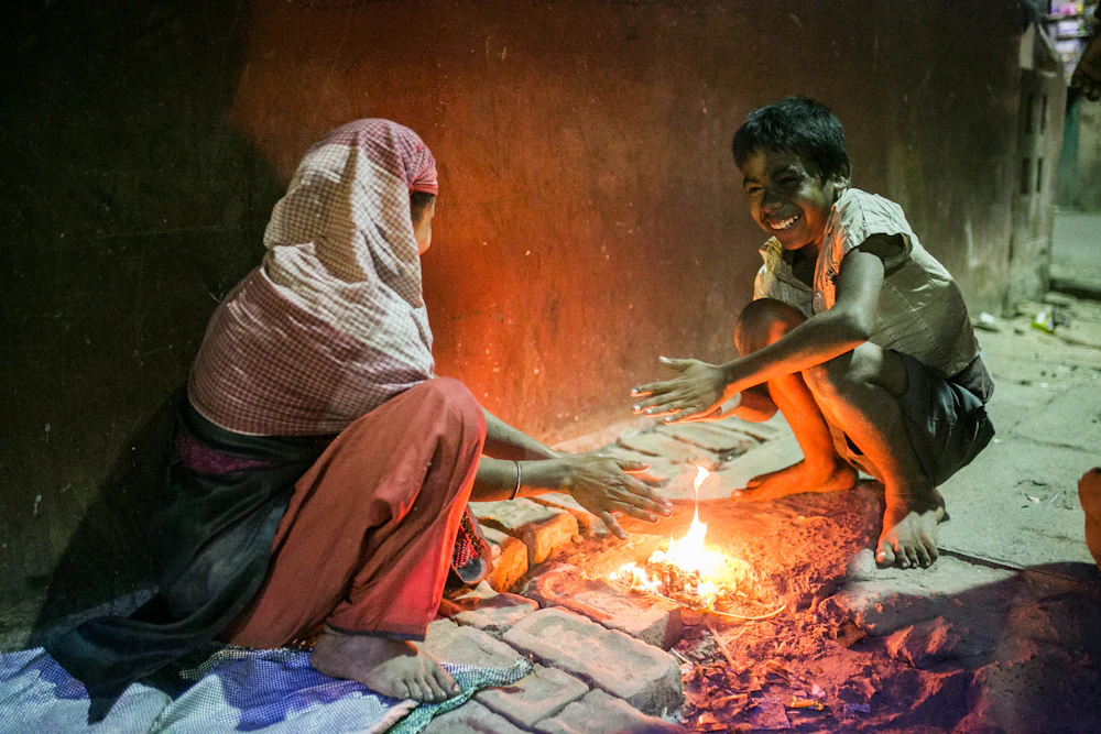 A cook tending a wood fire, lit by the glow of the embers