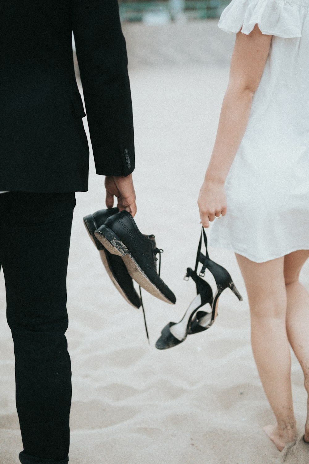 uomo e donna che camminano a piedi nudi sulla sabbia bianca tenendo scarpe e sandali