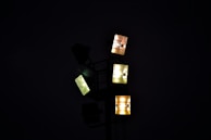 A cluster of illuminated floodlights against a dark background, forming geometric patterns with their square shapes. The lights emit a range of colors from yellow to white.