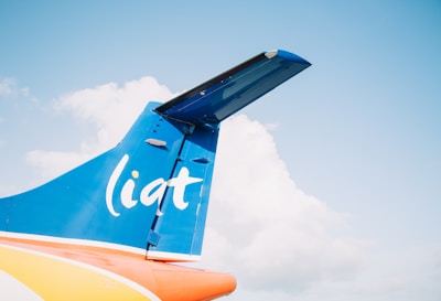 The image captures the tail section of a blue and orange airplane against a clear sky with some clouds. The airplane's tail features the word 'liat' in white letters.