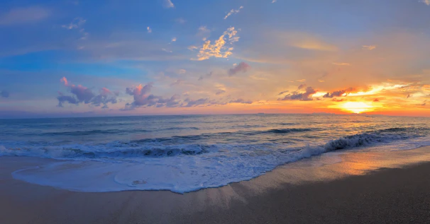 Sunset over a serene beach with gentle waves and colorful skies.