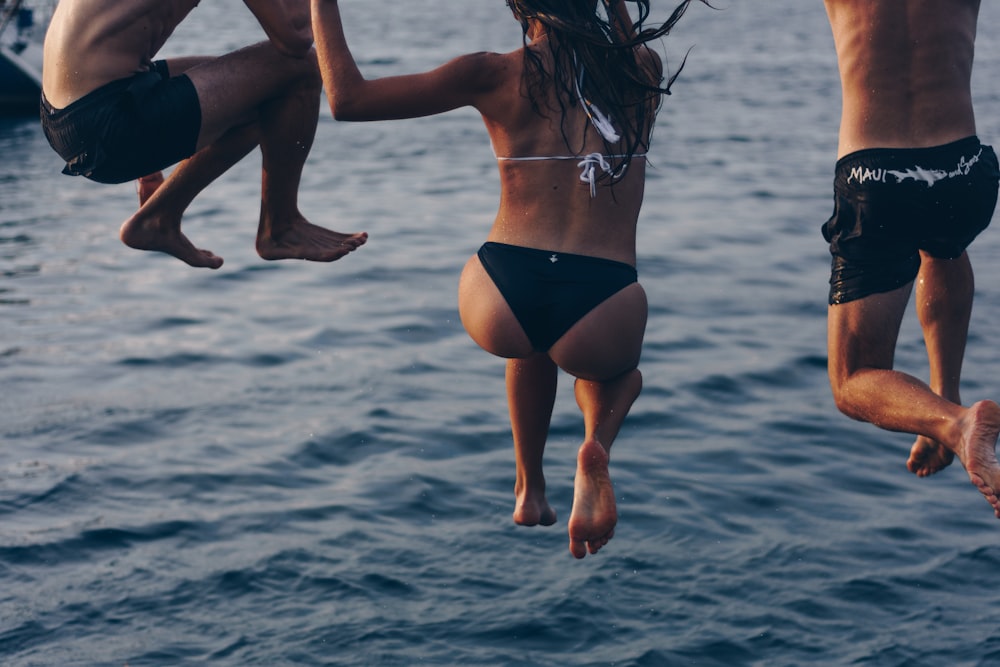 uma mulher e dois homens pulando no mar