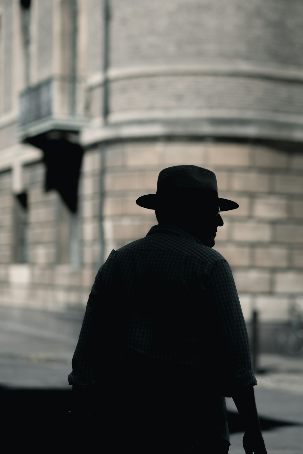 昼間、コンクリートの建物の近くに立っている帽子をかぶった男性のシルエット写真