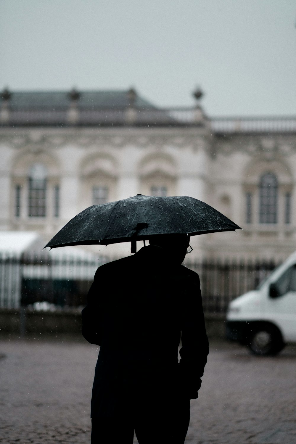 검은 우산을 들고있는 사람 흰색 차량 근처에 서있는 사람