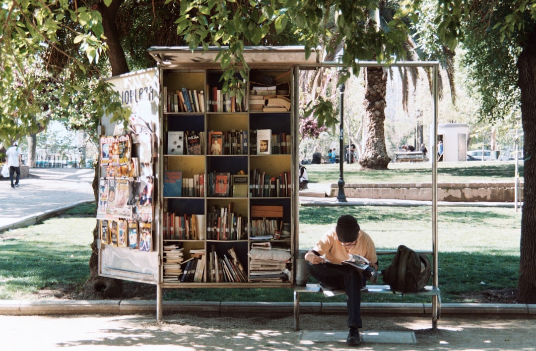 A man sitting on a bench next to a bookshelf in a park
