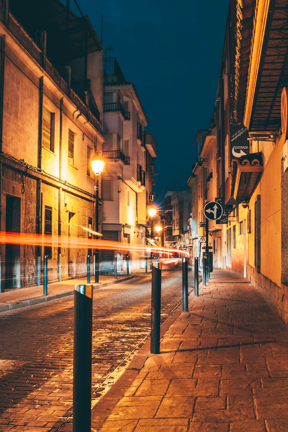 time-lapse photography of vehicle passing on the road between street lights and buildings during night time