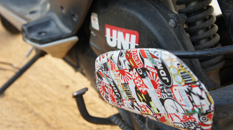 A close-up of colorful Kerala-themed stickers artfully arranged on a sleek laptop and a motorcycle helmet.