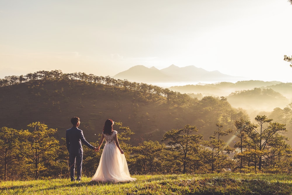 A married couple holds hands looking into the distance in a grassy wooded area in the Dalat hills