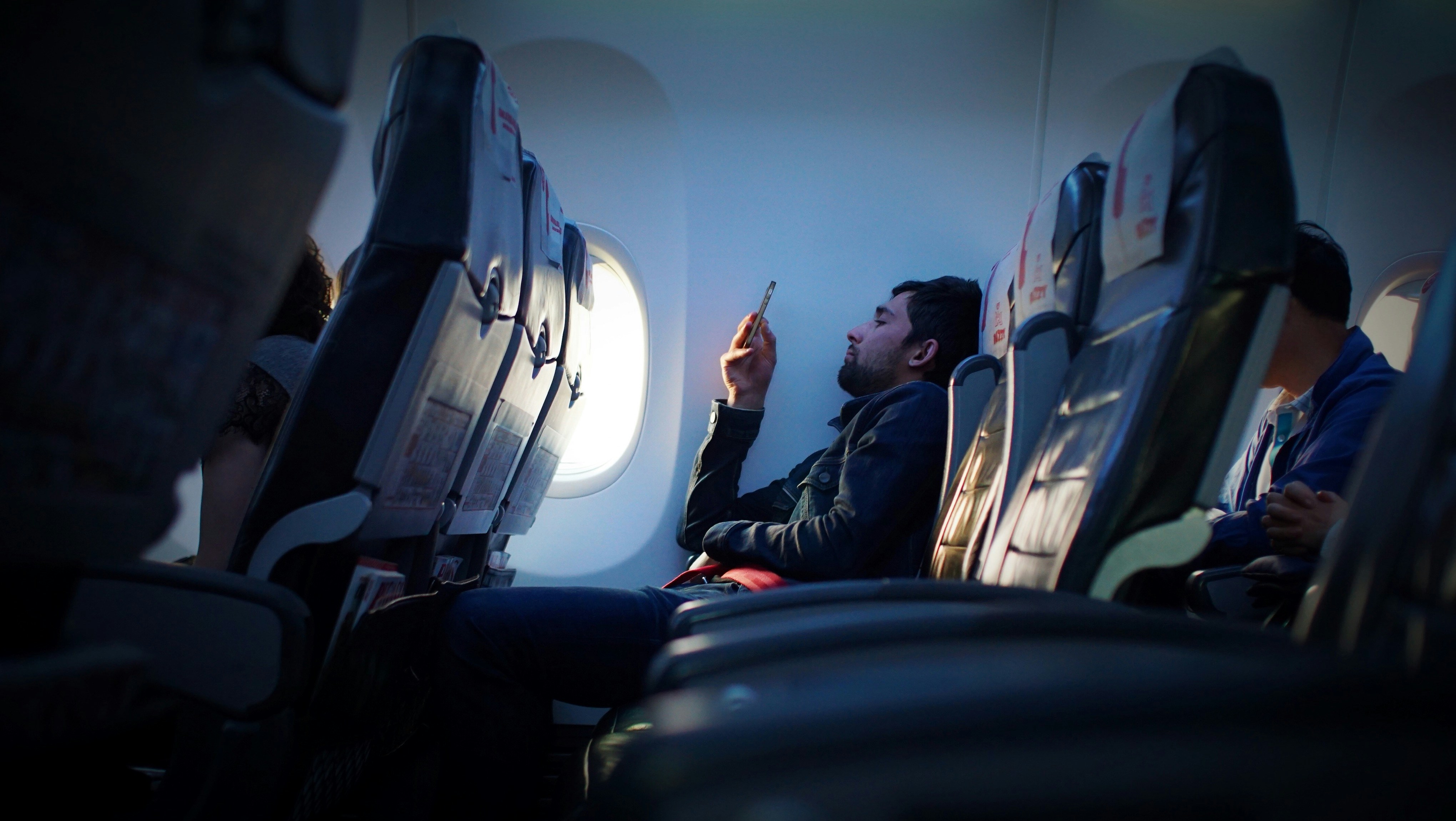 A bearded man using his phone on an airplane