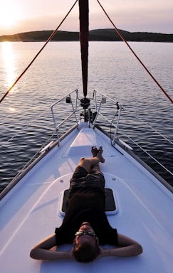 man lying on the bow of white boat in the ocean