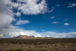 Wide shot of open desert land with rugged hills under a bright blue sky.