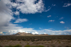 Wide shot of open desert land with rugged hills under a bright blue sky.
