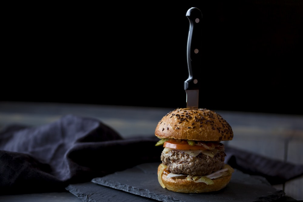 黒い布地の近くでナイフで串刺しにされたハンバーガー