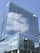 A modern glass office building reflecting the blue sky and clouds in its windows. The structure showcases a sleek and symmetrical design. A company logo is visible on the top corner of the building.