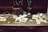 An antique wooden desk is adorned with vintage items including old photographs, a pair of black binoculars, a brown leather case, a marble with a wooden base, a decorative knife, and a small vase with flowers. The background consists of shelves filled with envelopes and papers.