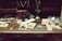 An antique wooden desk is adorned with vintage items including old photographs, a pair of black binoculars, a brown leather case, a marble with a wooden base, a decorative knife, and a small vase with flowers. The background consists of shelves filled with envelopes and papers.