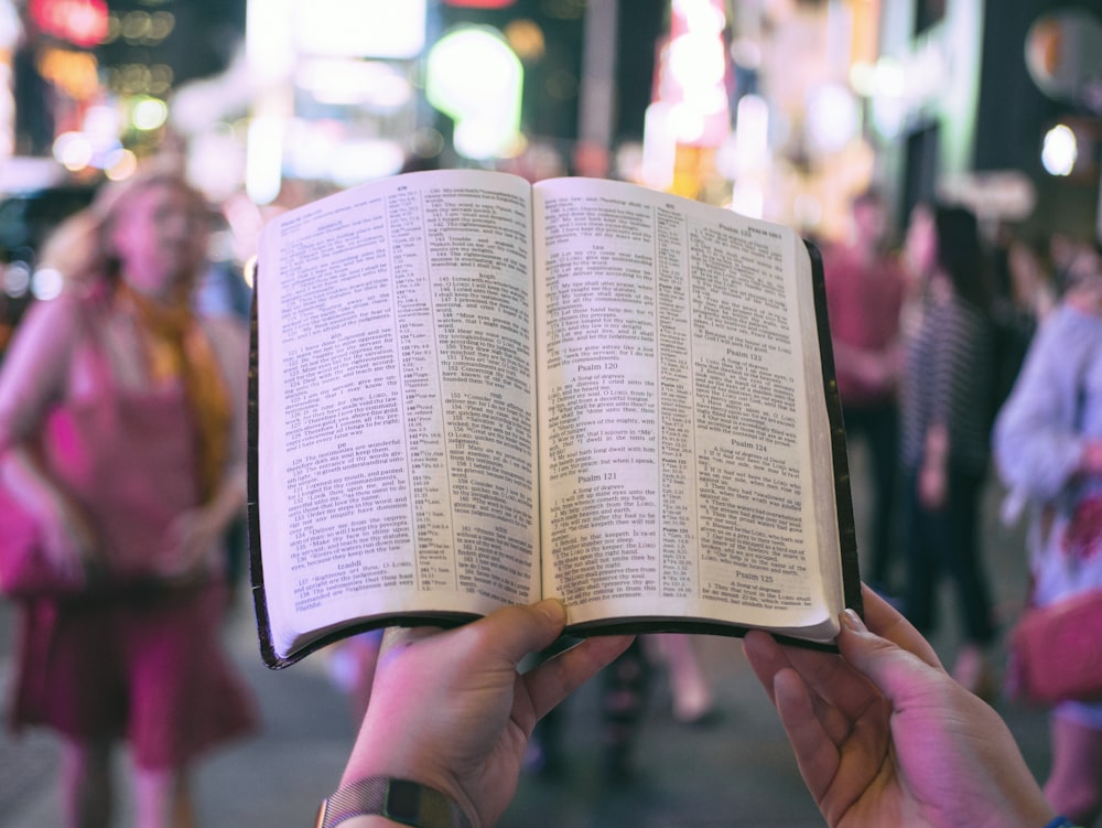 Person mit Bibel auf der Straße mit Menschen, die nachts auf dem Bürgersteig neben Gebäuden gehen