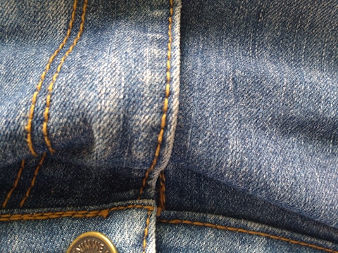 Close-up view of blue denim fabric featuring orange stitching details and a metal button.