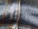 Close-up view of blue denim fabric featuring orange stitching details and a metal button.